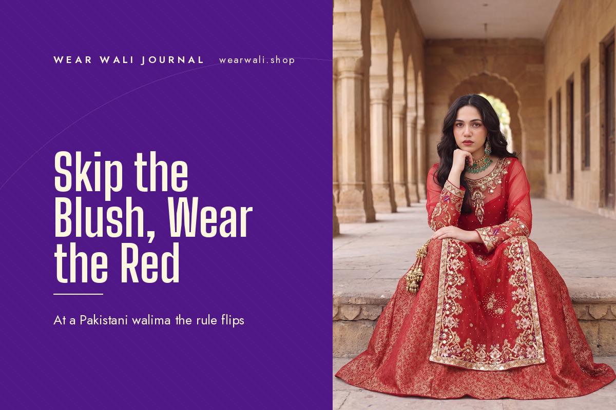 A woman in a red lehenga set with gold embroidery, seated on stone steps in an arched corridor.